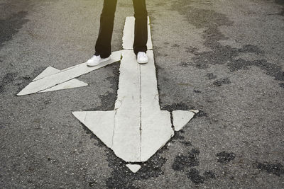 Low section of person with arrow sign on road