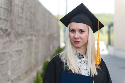 Portrait of woman wearing graduation gown standing outdoors