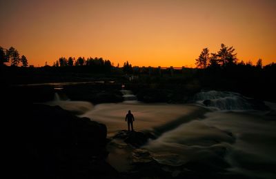 Silhouette man by trees against sky during sunset