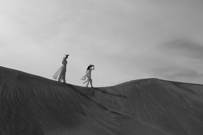 Women on sand dune in desert against sky