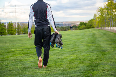 Low section of male athlete holding roller skates while walking on grass