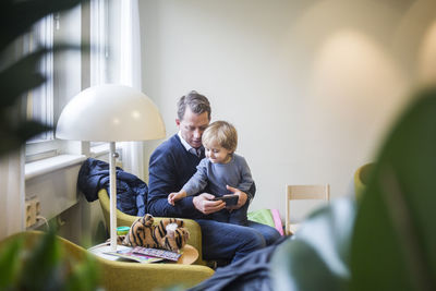 Father with smart phone while son looking at stuffed toy in hospital