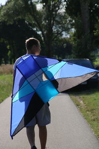 Rear view of man with kite walking on road