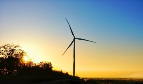Silhouette of wind turbines on field against sky during sunset