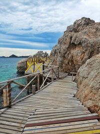 Walkway leading towards sea against sky