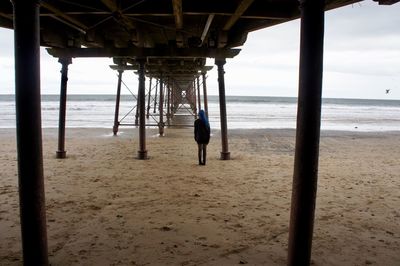 Rear view of woman standing at beach below pier