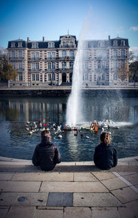People on fountain in city against clear sky