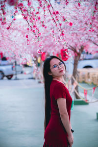 Portrait of smiling woman standing by pink cherry blossom