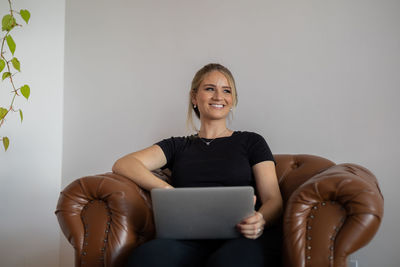 Portrait of young woman using laptop while sitting on sofa at home