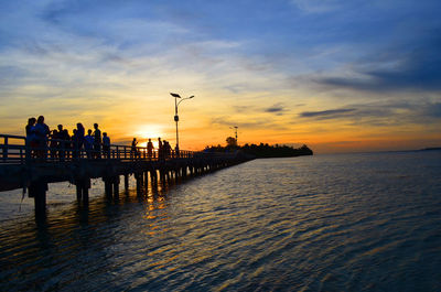 Silhouette people on pier over sea against sky during sunset