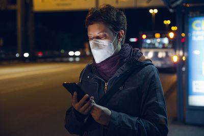 Young man using mobile phone in city at night