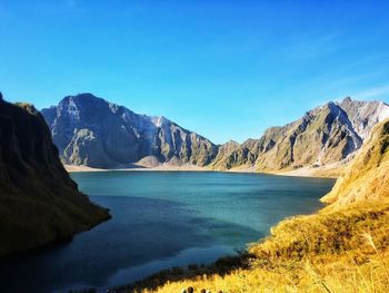 Scenic view of sea and mountains against clear blue sky