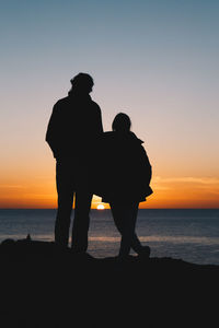 Rear view of silhouette man standing at beach against sky during sunset
