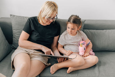 Young friends using phone while sitting on sofa at home