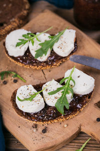 Bruschetta with fig jam, goat cheese and rucola on wooden plate.