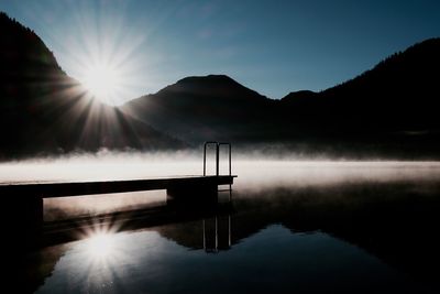 Scenic view of lake and silhouette mountains against sky at sunset