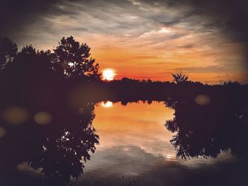 Silhouette trees by lake against sky during sunset