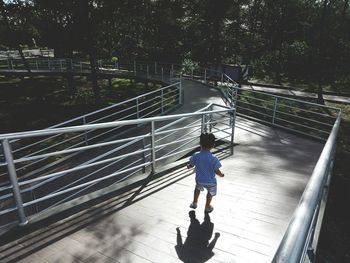 Rear view of boy walking on footbridge during sunny day