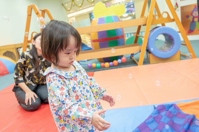 Cute girl with teacher on carpet in kindergarten