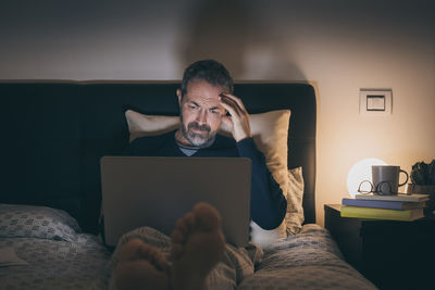 Man works with laptop lying on bed. male home working remote office. boy sit in bedroom use devices