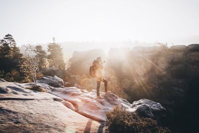 Full length of photographer photographing on rock against sky