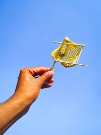 Low angle view of hand holding umbrella against clear blue sky