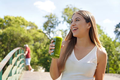 Beautiful healthy girl drinking kiwi mint kale green smoothie detox juice in city park
