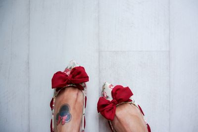 Low section of woman with tattoo wearing red bow shoes