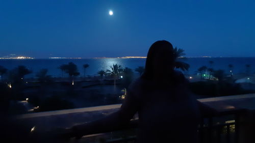Rear view of silhouette woman against illuminated city at night