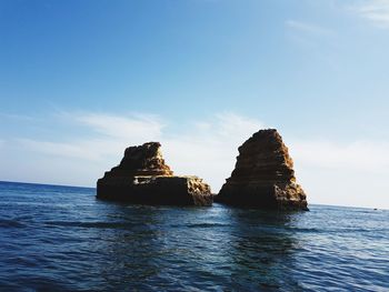 Rock formation by sea against blue sky