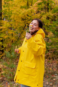 A cheerful young woman in a yellow raincoat and yellow boots on the background of an autumn