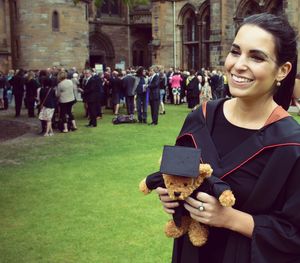 Young woman holding wearing graduation gown and holding teddy bear at university