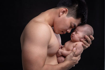 Midsection of man and baby against black background