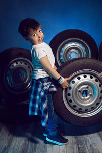 Boy in a white t shirt shirt and hat sits on a background of car wheels on a blue