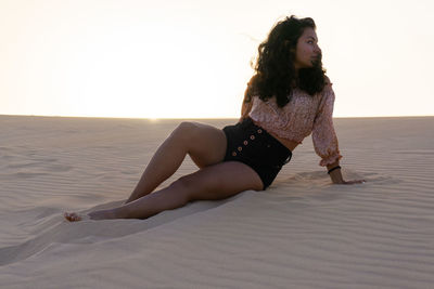 Young woman sitting on sand at desert against sky