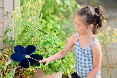 Young girl is watering plants in the backyard while wearing a bathing suit