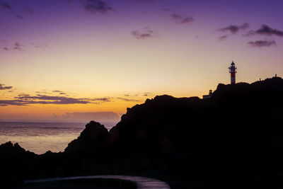 Silhouette of lighthouse at seaside during sunset
