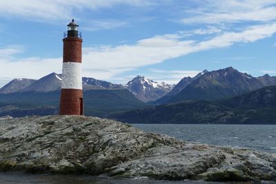 Lighthouse by sea and mountain against sky