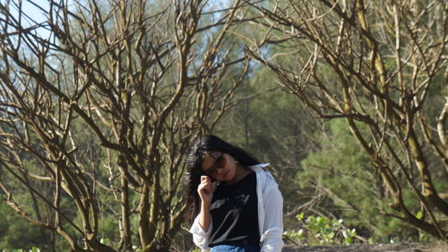 Young woman wearing sunglasses against trees at forest