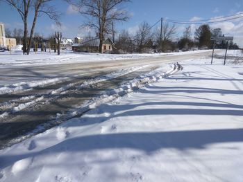 Snow covered field by road against sky