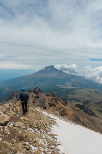 Rear view of man standing on snowcapped mountain against sky