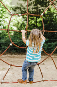 Rear view of girl playing on rope in playground