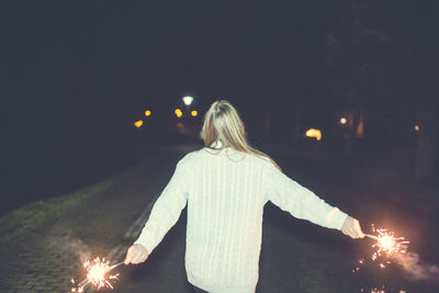 Rear view of women with sparklers against sky at night