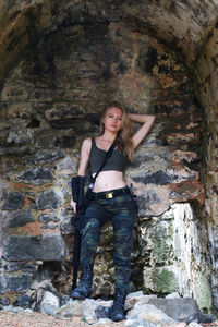 Portrait of woman with rifle standing against wall