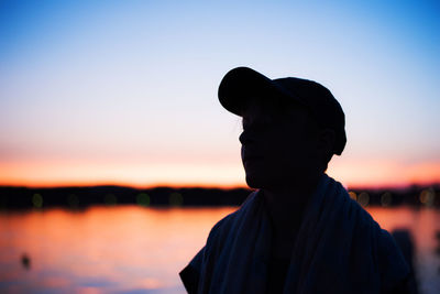 Side view of boy wearing cap against sky during sunset