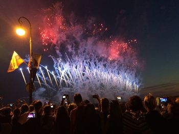 People looking at firework display during night