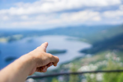 Cropped hand pointing against cloudy sky