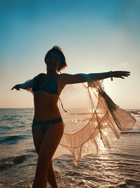 Young woman in white cover up dancing on the beach on sunset