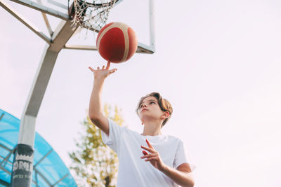 Low angle view of boy playing with basketball against sky