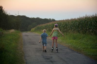 Rear view of brother helping sister in inline skating on road during sunset